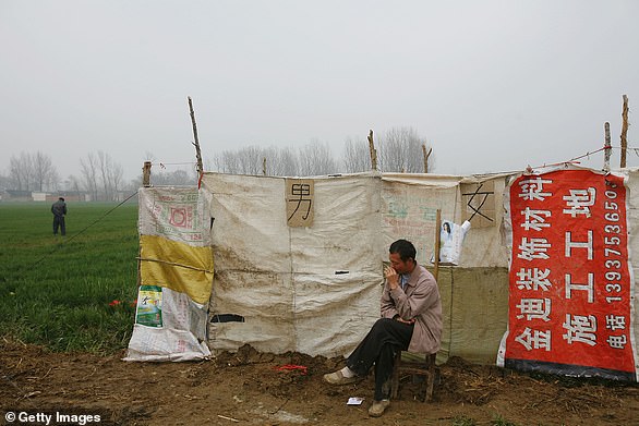 A villager sits in front of a tousy pay toilet in a wheat field in Henan province